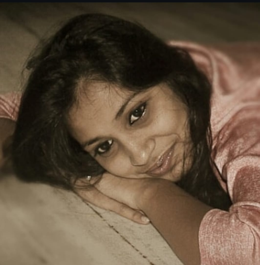 Young woman lying on the floor with her head resting on her arms, smiling softly at the camera.