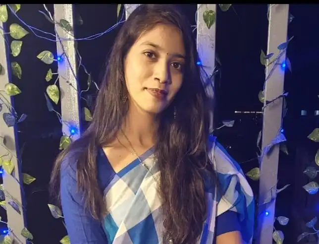 Woman wearing a blue and white saree posing gracefully at night with fairy lights in the background.